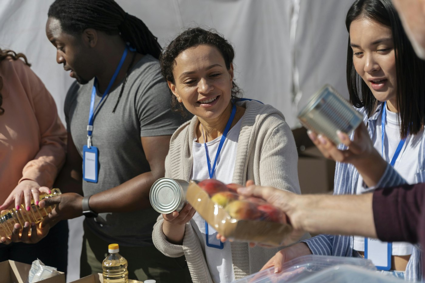 Volunteers with lanyards sort donated canned goods, cooking oil and fruit at a food drive table
