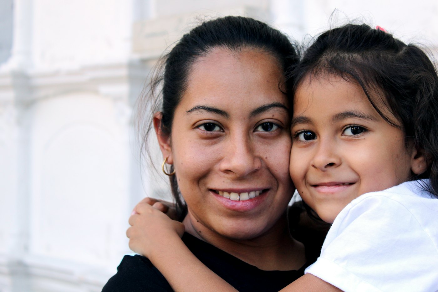 A smiling mother and young daughter hug cheek to cheek