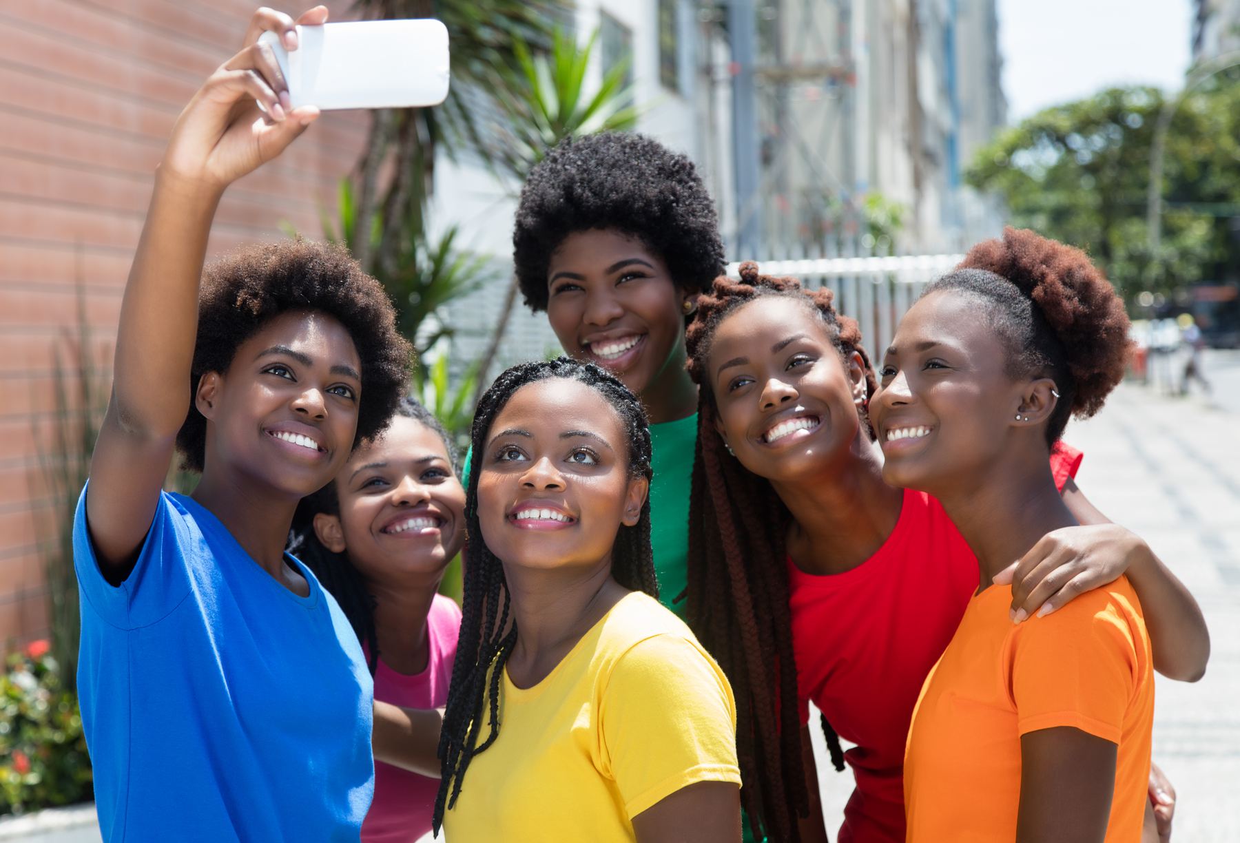 A group of smiling kids and young teens sit close together outdoors in warm sunlight