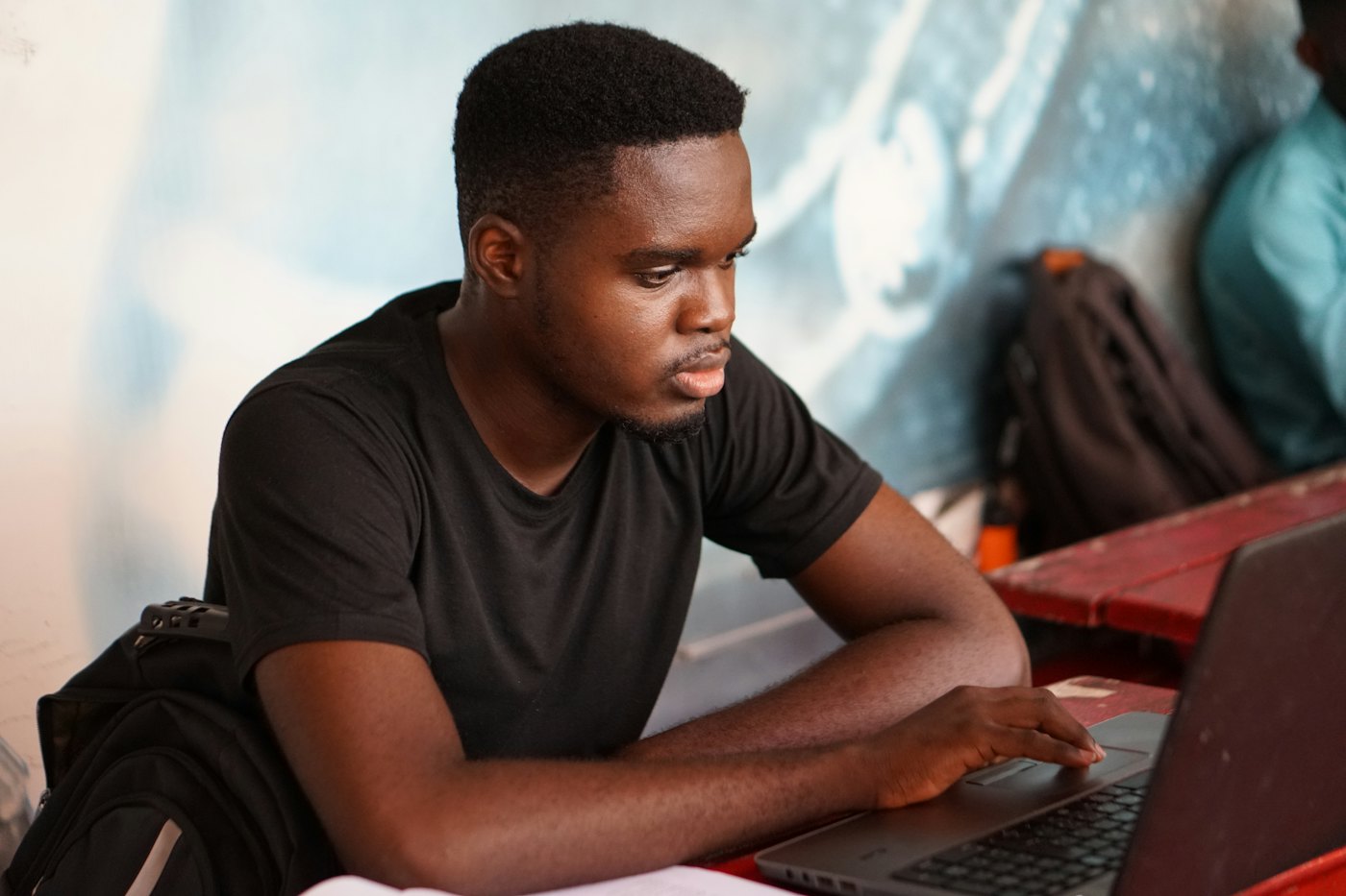 A young man in a black T-shirt works on a laptop