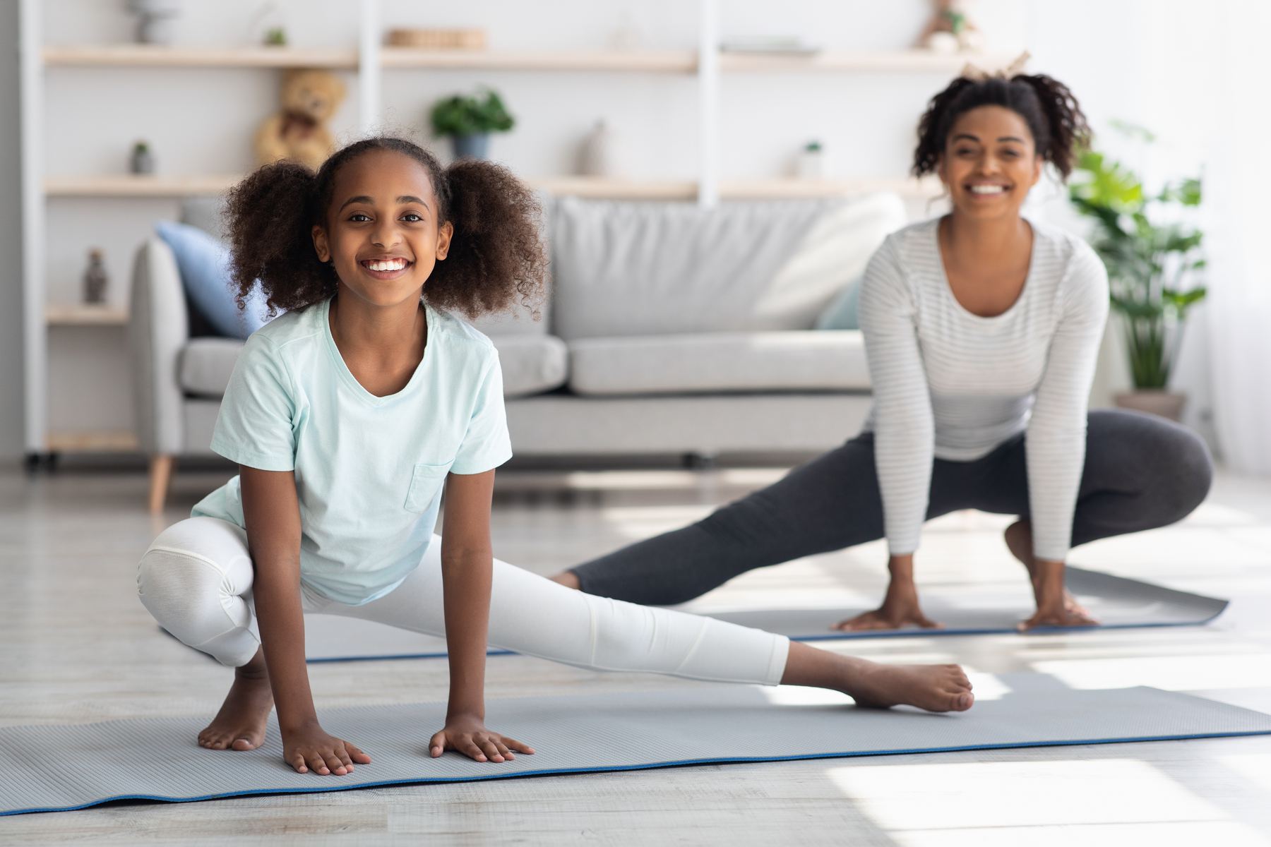 A smiling girl and a woman stretch together on yoga mats